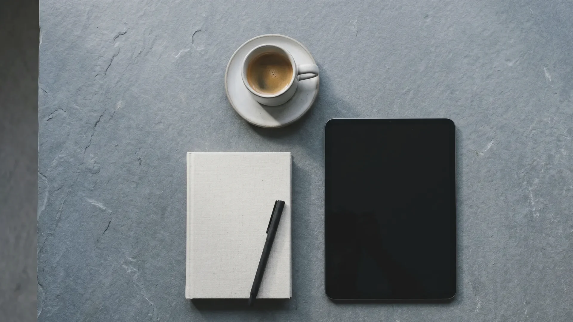 Detalle frío de una tableta y una libreta de notas sobre una mesa de pizarra